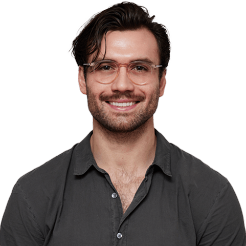 Smiling man with glasses and dark hair, wearing a dark button-up shirt, against a white background.