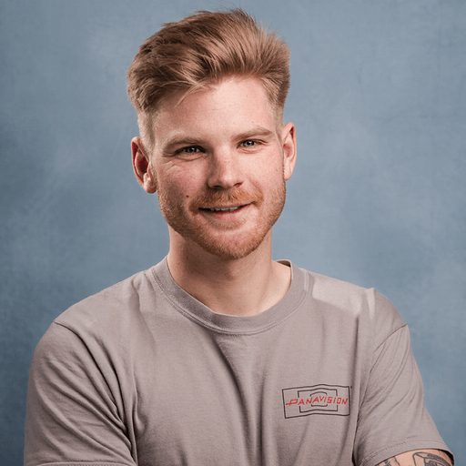 Smiling man with short hair and a beard wearing a gray Panavision T-shirt against a blue-gray background.