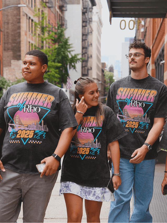 Three people walking on a city street, wearing matching "Summer of Rho 2023" shirts. They appear happy and relaxed.