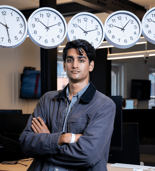 Person standing with arms crossed in an office, five clocks showing different times on the wall behind.