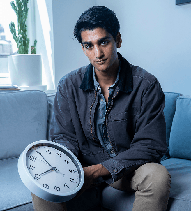 Person sitting on a couch holding a wall clock, with a potted plant in the background.