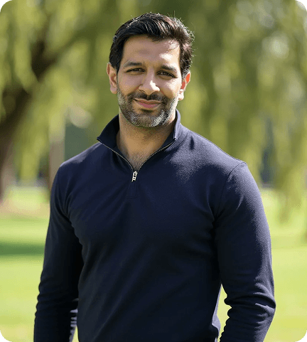 Man in a navy sweater stands outdoors on a sunny day, with a blurred green park background and trees.