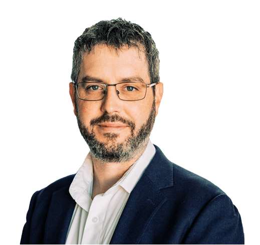 Man with glasses and a beard wearing a white shirt and dark blazer, smiling slightly against a plain background.